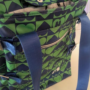 May include: Green and navy blue tote bag with a heart and geometric pattern. The bag has a blue shoulder strap, multiple pockets, and a zippered closure. The text "原花 lover" is visible on the side.