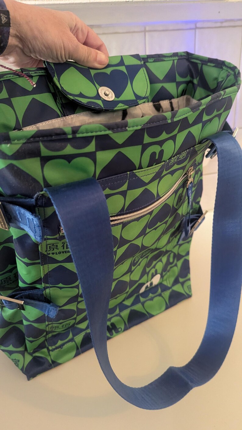 May include: Green and navy blue tote bag with a heart and geometric pattern. The bag has a blue shoulder strap, multiple pockets, and a zippered closure. The text "原花 lover" is visible on the side.