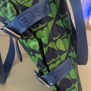 May include: A green and navy tote bag with a heart pattern. The bag has blue straps and the text "原宿" and "LOVERS" in white. The bag is made of a shiny material and has silver hardware.