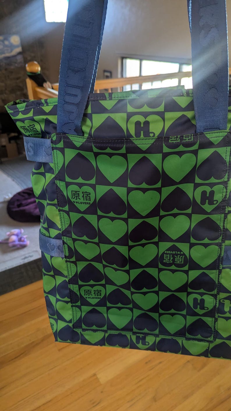 May include: Green and navy tote bag with a repeating heart pattern. The bag features a navy blue strap and the text "原宿" and "W LOVERS" in white. The bag has a square shape.