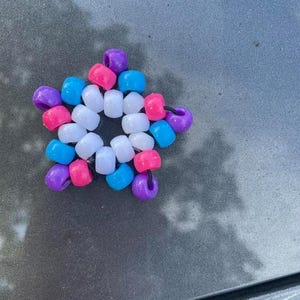 Op de afbeelding: Een kleurrijke stervormige kralenarmband met witte, roze, blauwe en paarse kralen.