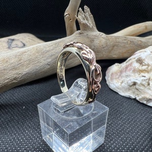 May include: A gold and rose gold ring with a swirling, organic design. The ring is on a display stand.