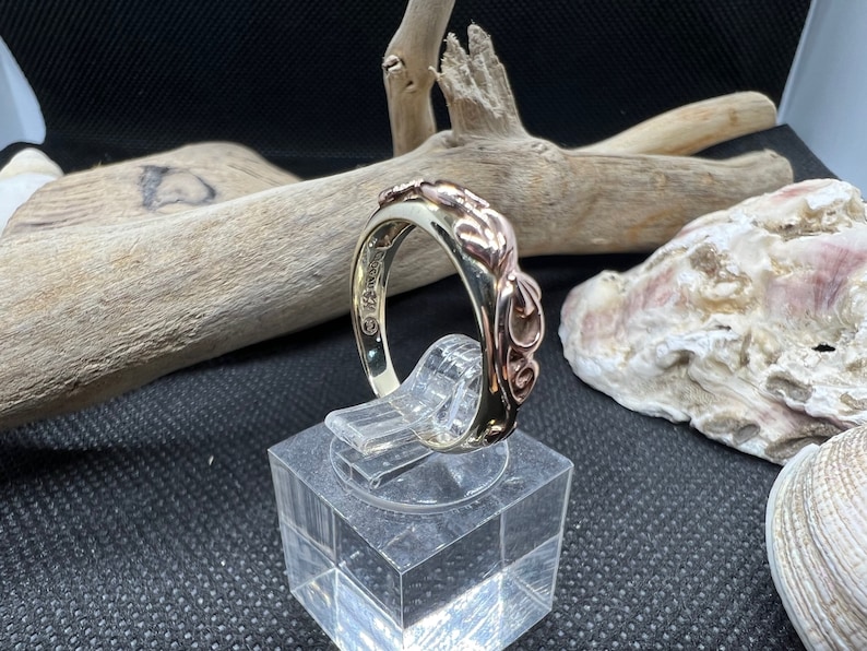 May include: A gold and rose gold ring with a swirling, organic design. The ring is on a display stand.