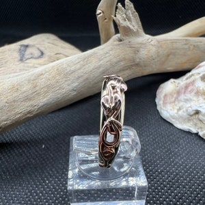 May include: A gold ring featuring an intricate design of interlaced hearts and leaves. The ring is crafted from two distinct shades of gold, resulting in a sophisticated and stylish piece.