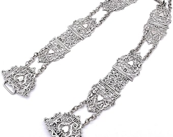 May include: A silver filigree chain belt with multiple decorative links. The belt is made of intricate, openwork designs with a heart motif.