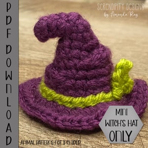 May include: A purple crocheted witch's hat with a green brim and a green leaf detail. The hat is small and is sitting on a wooden surface. The text "MINI WITCH'S HAT ONLY" is printed on a gray background.