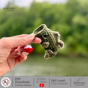 May include: Crocheted green fish keychain with a black eye and a red and white bobber charm. The keychain is handmade and features the text "SERENDIPITY DESIGNS by Amanda Ray".