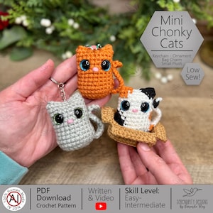 May include: Three crocheted cat charms in orange, gray, and calico patterns. Each cat has large, expressive eyes and is designed as a keychain or bag charm. The image includes text that says "Mini Chonky Cats".