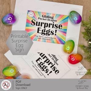 Puede incluir: Imagen de huevos sorpresa coloridos y un letrero imprimible. El letrero dice "Gliding Pocket Dragon Surprise Eggs!" con el texto "Tiny, fierce, and ready for epic adventures!" Los huevos son en tonos morado, verde y naranja.