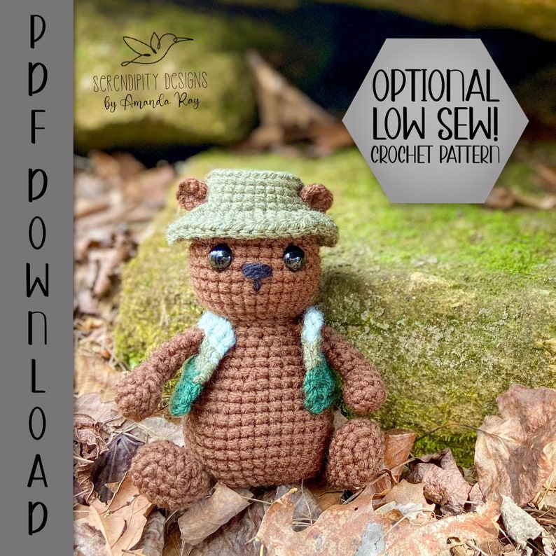Pu&ograve; includere: Un orso di peluche marrone che indossa un gilet verde e blu e un cappello verde. L'orso &egrave; seduto su un letto di foglie marroni. Il testo "OPTIONAL LOW SEW! CROCHET PATTERN" &egrave; nell'angolo in alto a destra dell'immagine.