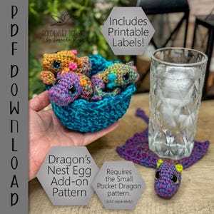 Könnte beinhalten: Ein gehäkeltes Drachennest mit drei kleinen Drachen in einem blauen Korb. Die Drachen sind mehrfarbig mit großen Augen. Ein Glas Wasser und ein Drachenuntersetzer sind ebenfalls zu sehen. Der Text auf dem Bild lautet "Dragon's Nest Egg Add-on Pattern".