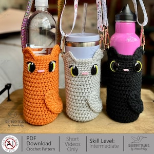 May include: Three crochet water bottle holders in orange, gray, and black, each shaped like a cat with large eyes and a pink nose. The holders have straps for carrying and are designed to fit various bottle sizes. The bottles are visible inside the holders.