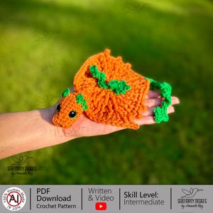 May include: An orange and green crocheted dragon with black eyes. The dragon is handmade and features a detailed design. The image also includes text that says "PDF Download Crochet Pattern" and "Written & Video". The skill level is listed as "Intermediate".