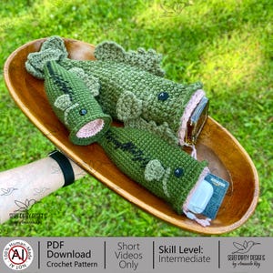 May include: Crocheted green fish-shaped pouches with pink interiors and black accents. One pouch holds a gift card and earbuds. The pouches are displayed in a wooden bowl on a green grassy surface. The text on the image says "PDF Download Crochet Pattern".