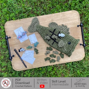 May include: A wooden serving tray displays a collection of handmade crochet items. The centerpiece is a large green fish with a tic-tac-toe game. Other items include fish-shaped earrings, keychains, and small fish. A black pen and tags are also present.