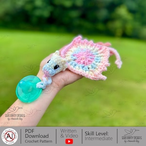 Peut inclure: Un porte-sucette en forme de dragon au crochet fait à la main, aux couleurs pastel. Le dragon a une tête bleue et blanche, un corps rose et bleu et une sucette verte. Le patron de crochet est disponible en téléchargement PDF.