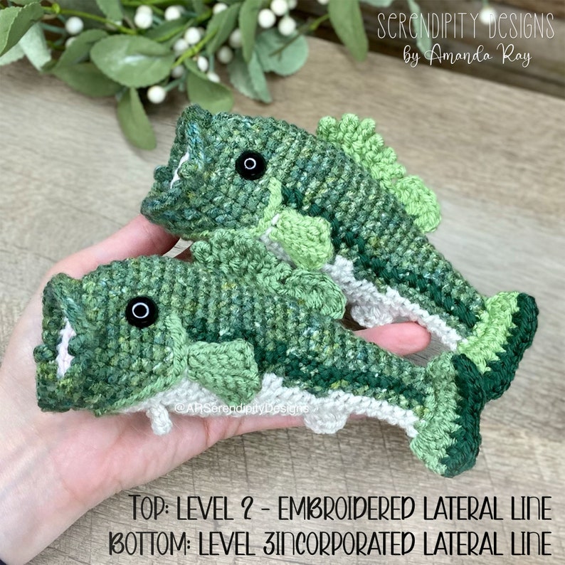 May include: Two handmade crochet fish in shades of green, with black eyes and open mouths. The fish have white and gray accents. The text at the bottom reads: TOP: LEVEL 2 - EMBROIDERED LATERAL LINE BOTTOM: LEVEL 3 INCORPORATED LATERAL LINE.
