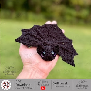 May include: A black crochet bat with large, purple eyes. The bat's wings are spread, and the body is detailed with textured crochet stitches. The image includes text that says "Serendipity Designs by Amanda Ray" and "PDF Download Crochet Pattern".