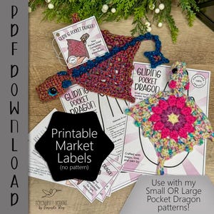 Peut inclure: Un dragon fait à la main au crochet dans les tons de rouge, de bleu et de rose, avec un charme en forme d'étoile. L'image comprend des étiquettes imprimées avec le texte "Gliding Pocket Dragon" et "Printable Market Labels".