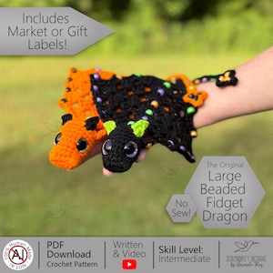 May include: Two crocheted dragon fidget toys, one orange and one black, are displayed. The black dragon has green accents and purple eyes. The orange dragon has black accents and black eyes. The text on the image says "The Original Large Beaded Fidget Dragon".