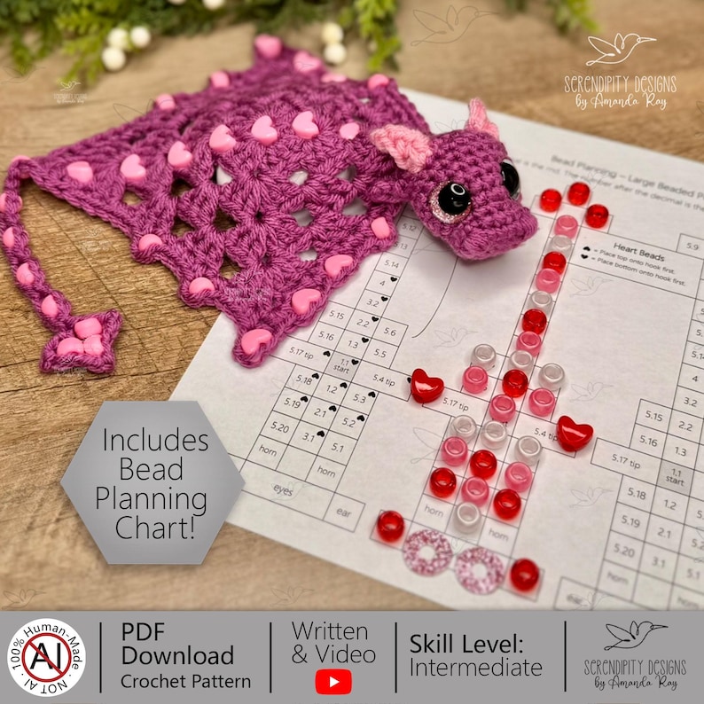 May include: A handmade crochet bookmark in shades of purple, adorned with pink heart-shaped beads. The bookmark features a dragon design with a matching crochet head. A bead planning chart and other craft supplies are also visible.