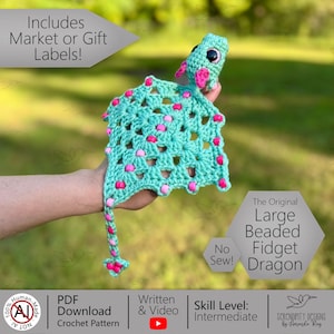 May include: A turquoise crocheted dragon with pink accents and beaded details. The dragon has large eyes and a long tail. The text on the image says "The Original Large Beaded Fidget Dragon".