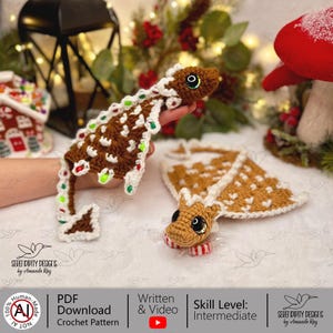 May include: Crocheted gingerbread lizard ornaments with white, red, and green accents. One lizard is held up, and another lies flat. The ornaments have large, expressive eyes and are decorated with candy-like details. The crochet pattern is available as a PDF download.