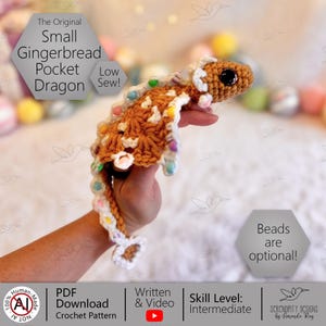 May include: A crocheted gingerbread dragon in shades of brown, white, and pastel colours. The dragon has a detailed, textured design with bead accents. Text on the image reads "The Original Small Gingerbread Pocket Dragon".