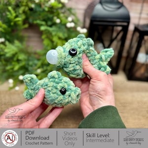 May include: Two handmade crochet fish in shades of green, with black safety eyes and a bubble. The fish are made with a textured yarn. The image includes text that says "PDF Download Crochet Pattern" and "Short Videos Only".