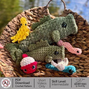 May include: A collection of handmade crochet toys, including green fish, a yellow creature, a pink worm, a red and white bobber, and a blue and white lure, all nestled in a woven basket. The image includes text that says "PDF Download Crochet Pattern".