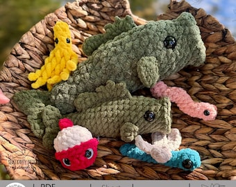 May include: A collection of handmade crochet toys, including green fish, a yellow creature, a pink worm, a red and white bobber, and a blue and white lure, all nestled in a woven basket. The image includes text that says "PDF Download Crochet Pattern".