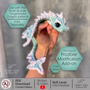 Peut inclure: Un dragon crocheté bleu et blanc, avec de grands yeux sombres. Le dragon est présenté, mettant en valeur son design détaillé. Le texte sur l'image indique "The Original Frostbite Modification Add-on" et "Low Sew!"
