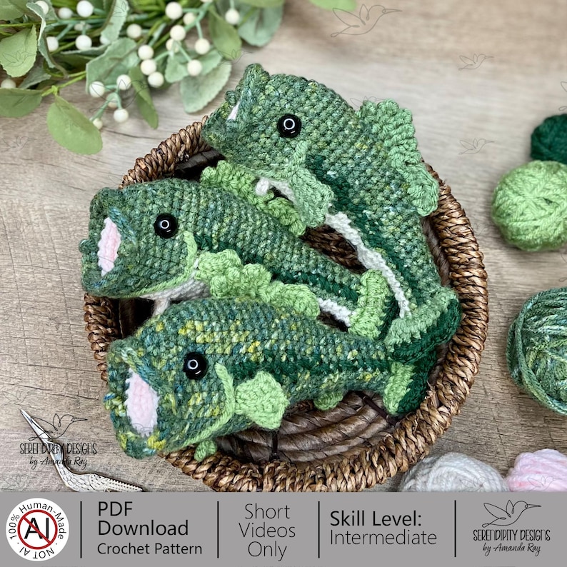May include: Three handmade crochet fish in a woven basket. The fish are primarily green with black eyes and white and pink accents. The basket is brown, and the background includes greenery and yarn. The fish are a unique handmade item.