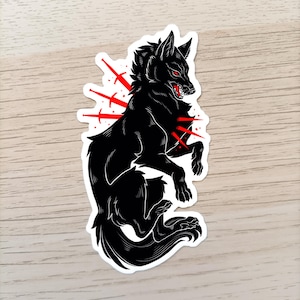 Puede incluir: Pegatina de lobo negro con detalles rojos. El lobo se representa en una pose estilizada y agresiva con ojos rojos y una boca gru&ntilde;ona. L&iacute;neas rojas emanan del cuerpo del lobo, creando un efecto visual impactante. La pegatina tiene un borde blanco.