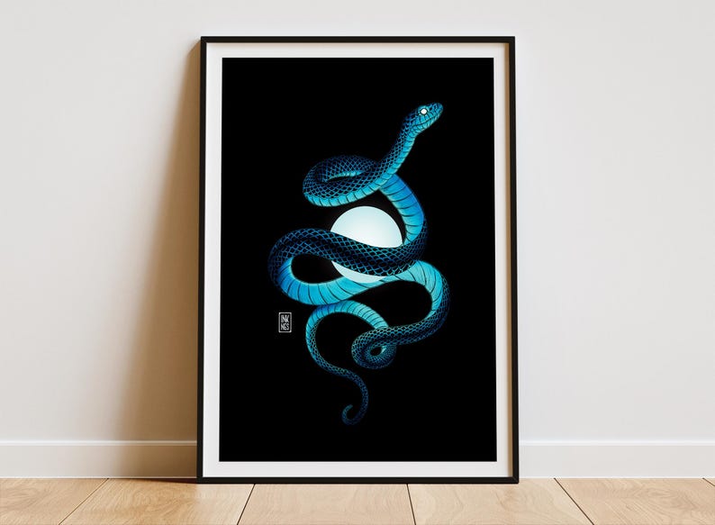 Art print of a coiled blue snake wrapped around a glowing orb of light. The background is solid black, creating a dramatic contrast with the snake and the soft glow from the orb. The print is framed in a thin black frame. The frame is placed on a light wooden floor rested against a white wall.