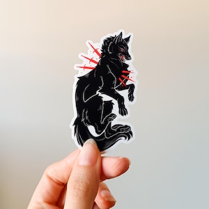 Puede incluir: Pegatina de lobo negro con detalles rojos. El lobo est&aacute; representado en una pose din&aacute;mica, con explosiones rojas que emanan de su cuerpo. La pegatina tiene un borde blanco.