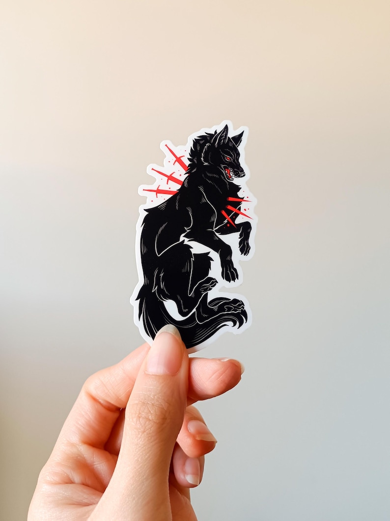 Puede incluir: Pegatina de lobo negro con detalles rojos. El lobo est&aacute; representado en una pose din&aacute;mica, con explosiones rojas que emanan de su cuerpo. La pegatina tiene un borde blanco.