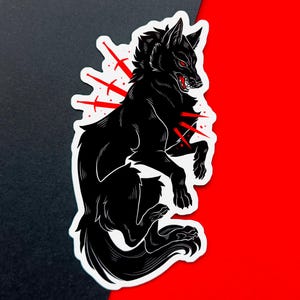 Black wolf sticker snarling with three re swords piercing through its chest. Fierce gothic animal illustration. The sticker is placed on overlapping red and black cardstock, enhancing its bold gothic aesthetic.