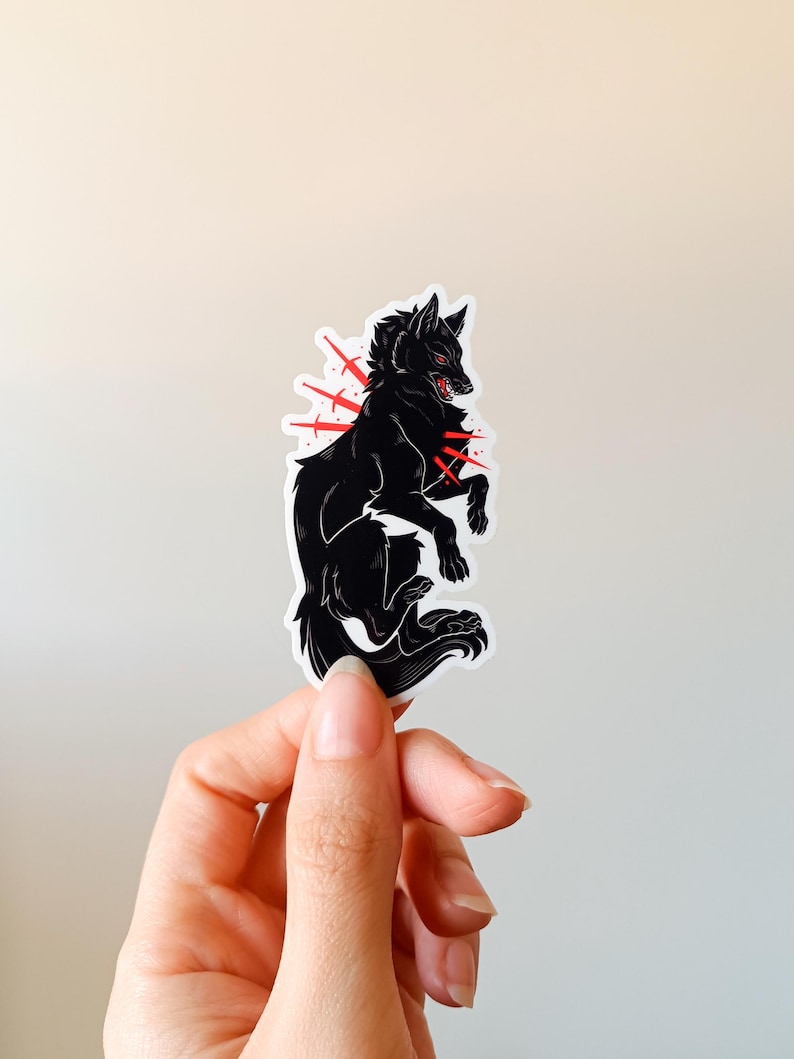 Puede incluir: Una pegatina de lobo negro con detalles en rojo. El lobo est&aacute; representado en una pose din&aacute;mica, con la boca abierta y los ojos rojos. Explosiones rojas emanan del pecho del lobo, a&ntilde;adiendo un efecto dram&aacute;tico. La pegatina se sostiene sobre un fondo neutro.