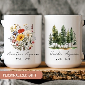 May include: Two white ceramic mugs with black handles and black rims. The mug on the left has a floral design and the text "Auntie Again ♥ EST. 2024". The mug on the right has a watercolor design of pine trees and the text "Uncle Again ♥ EST. 2024".