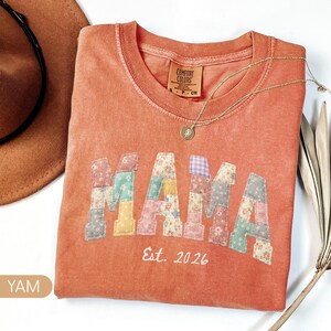 Personalized Comfort Colors yam shirt with custom floral patchwork name text, folded flat lay with boho hat and necklace, perfect grandma, nana, mimi, or mama birthday gift tee.
