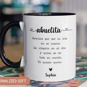 Pode incluir: Caneca de cer&acirc;mica branca com al&ccedil;a e borda pretas. A caneca apresenta a palavra "abuelita" em escrita cursiva, juntamente com uma mensagem sincera em espanhol e o nome "Sophia". A caneca &eacute; um presente personalizado.