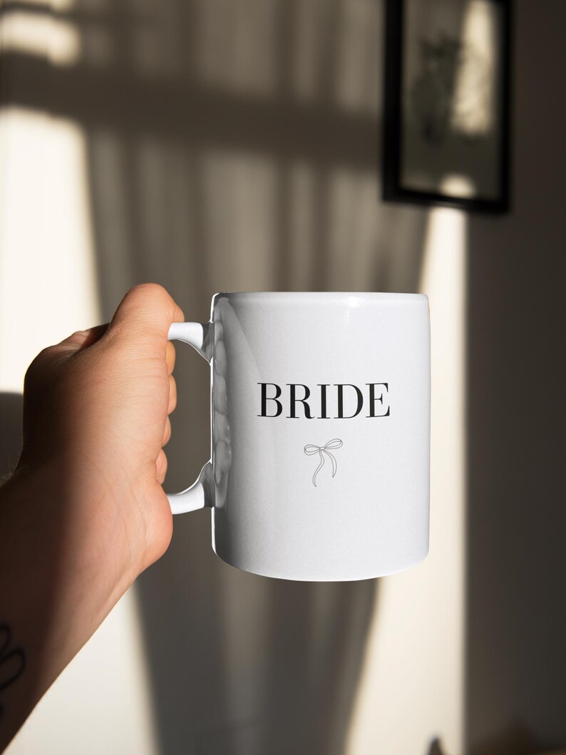 May include: White ceramic mug with a black inscription that reads "BRIDE" and a small black bow.