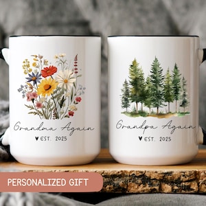 May include: Two white ceramic mugs with black handles and rims. The mug on the left has a floral design and the text "Grandma Again est. 2025". The mug on the right has a forest scene and the text "Grandpa Again est. 2025".