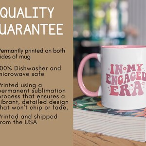 May include: White ceramic mug with a pink rim and handle. The mug has a pink and white graphic that says "In My Engaged Era" with a small ring and star design.