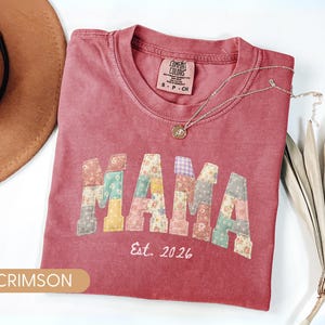 Personalized Comfort Colors crimsom shirt with custom floral patchwork name text, folded flat lay with boho hat and necklace, perfect grandma, nana, mimi, or mama birthday gift tee.