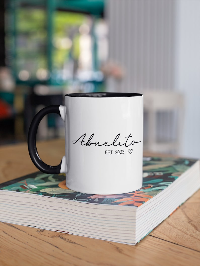 May include: White ceramic mug with a black handle and black rim. The mug has the text "Abuelito Est. 2023" in black script.