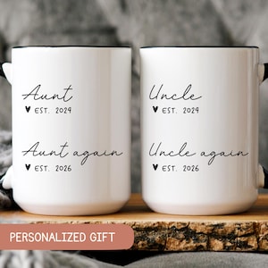 May include: Two white ceramic mugs with black handles. One mug reads "Aunt EST. 2024 Aunt again EST. 2026". The other mug reads "Uncle EST. 2024 Uncle again EST. 2026". The mugs are on a wooden surface with a "PERSONALIZED GIFT" banner.