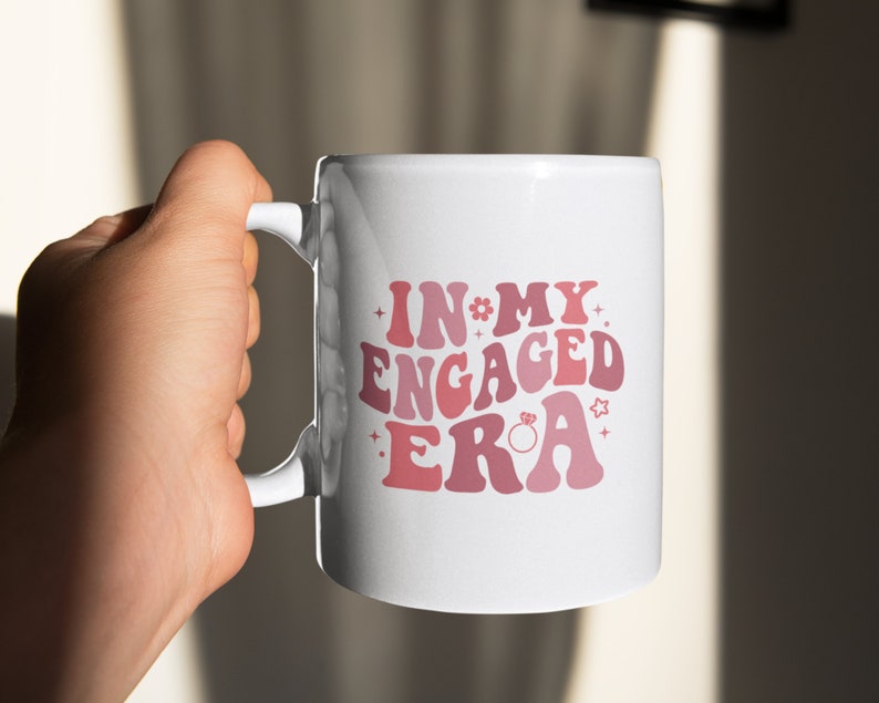 May include: White ceramic mug with a pink and red graphic that says "In My Engaged Era" with a small ring graphic.
