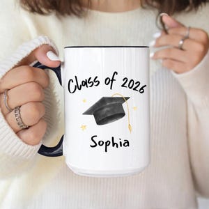 White and black ceramic mug with a black graduation cap and the text "Class of 2026" and "custom name" in black.